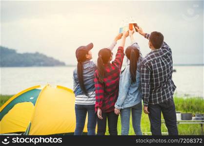 Back view of friendship clinking drinking bottle glass for celebrating in private party with mountain and lake view background. People lifestyle and travel on vacation concept. Picnic and camping tent