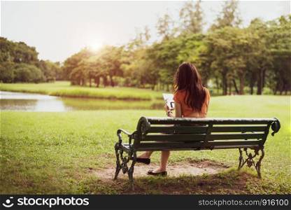 Back view of happy beauty woman in casual outfits using tablet in national park background. People lifestyles and technology concept. Nature and relaxation theme. Summer and autumn seasonal theme.