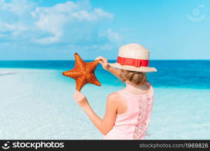 Back view of kid on the beach. Adorable little girl with starfish on white empty beach