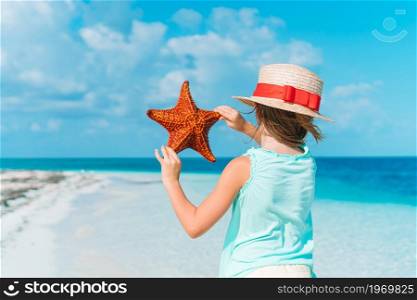 Back view of kid with starfish on white empty beach. Adorable little girl with starfish on white empty beach