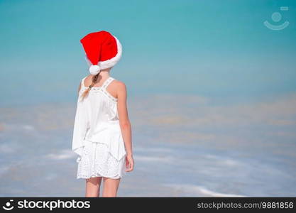 Back view of little girl in red Santa hat on tropical beach on Christmas vacation. Adorable little girl in Santa hat on tropical beach