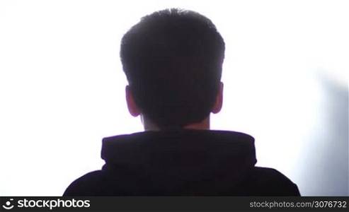 Back view of man&acute;s silhouette listening to music with headphones against white background. Man putting on wireless bluetooth technolgy headphones and listening to rock music. Head moving to follow the beat.