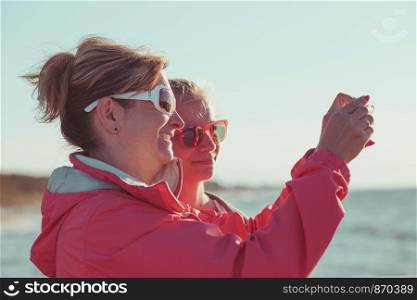 Back view of mother and her daughter taking a photos over sea during summer vacation using smartphone camera