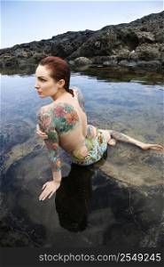 Back view of nude sexy Caucasian tattooed woman in bikini lying in tidal pool in Maui, Hawaii, USA.