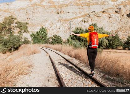 Back view of professional female hiker with tourist backpack exploring wilderness environment during hiking trekking on railway to discover new places. Back view of professional female hiker with tourist backpack exploring wilderness environment during hiking trekking on railway.