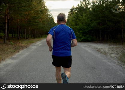 Back view of senior man running outside among countryside road. Healthy lifestyle and physical activity for wellness on retirement. Back view of senior man jogger performing exercise outside among countryside road