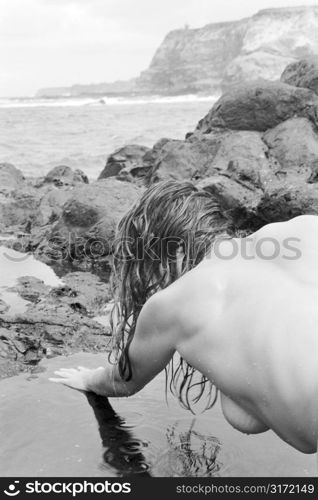 Back view of sexy nude Caucasian woman in tidal pool in Maui, Hawaii.