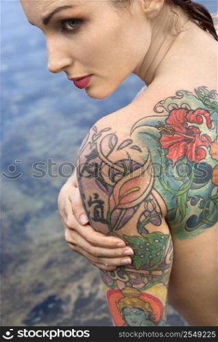 Back view of sexy nude tattooed Caucasian woman by tidal pool in Maui, Hawaii, USA.