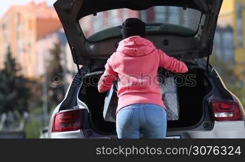 Back view of stylish woman putting shopping bags into the trunk of car after shopping day.