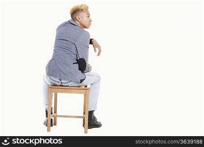Back view of teenage boy sitting on chair as he looks away over gray background