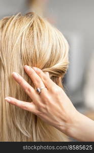 Back view of the female hand of hairdresser models a hairstyle of a young blonde woman in a hair salon. Hairdresser models hairstyle of woman