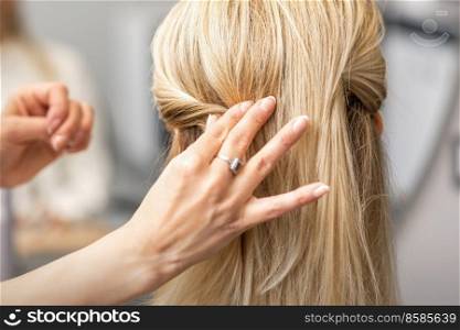 Back view of the female hand of hairdresser models a hairstyle of a young blonde woman in a hair salon. Hairdresser models hairstyle of woman