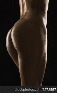 Back view of thighs and buttocks of nude Hispanic mid adult woman glistening with body oil.