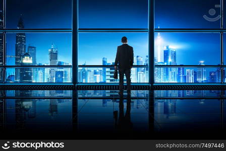 Back view of thoughtful businessman looking out of big office window at office ,planning future project concept, night scene .