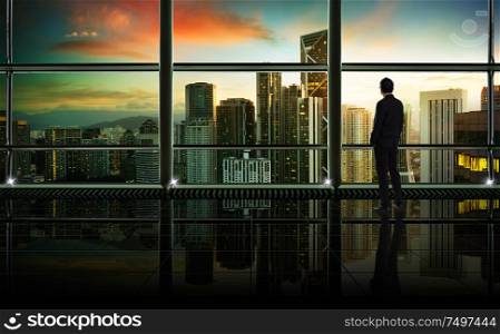 Back view of thoughtful businessman looking through window at big modern city,planning future project concept, early morning scene .