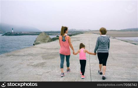 Back view of three female generations walking by sea pier. Back view of three female generations walking