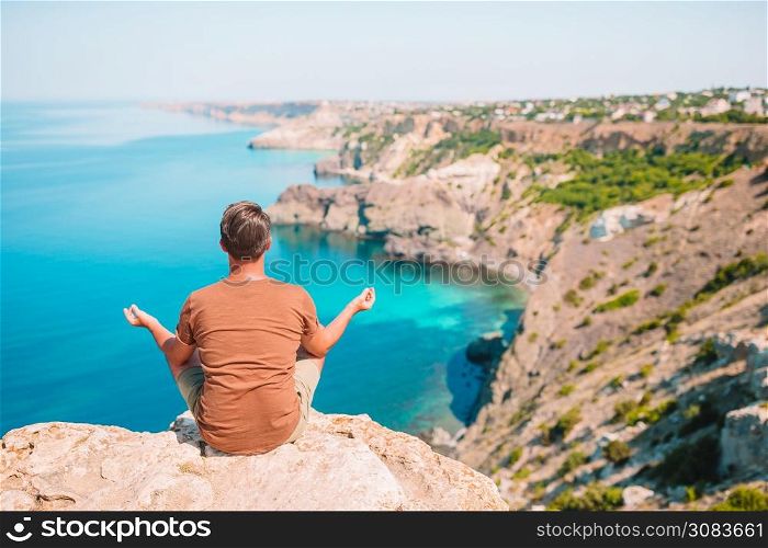 Back view of tourist man in meditation outdoor on edge of cliff. Tourist man outdoor on edge of cliff seashore