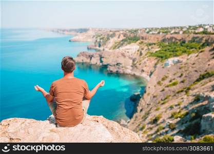 Back view of tourist man in meditation outdoor on edge of cliff. Tourist man outdoor on edge of cliff seashore