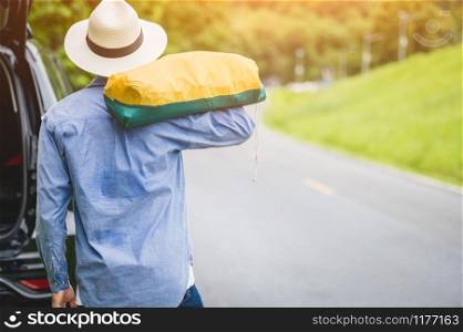 Back view of tourist walking along road with bag during travel in countryside. People lifestyles and vacation concept. Man holding and backpack for long holiday trip with mountain background