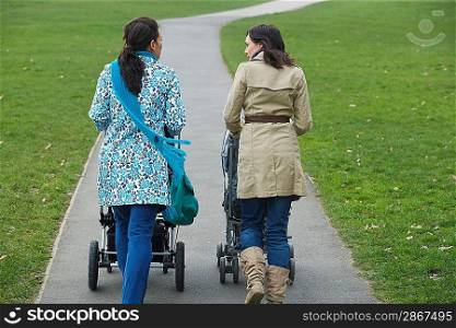 Back view of two mothers pushing strollers in park