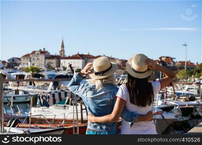 Back view of two tourists looking at old european city, boats, marina and resort.