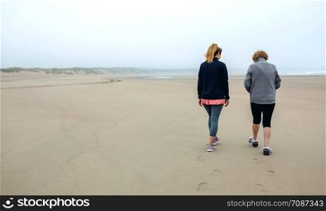 Back view of two women walking on the beach in autumn. Two women walking on the beach