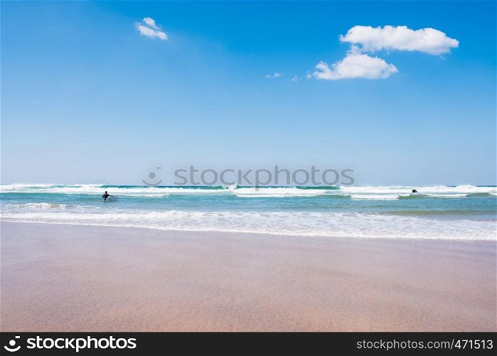 back view of unidentified man with surf board in blue ocean water. Summer beach panoramic view
