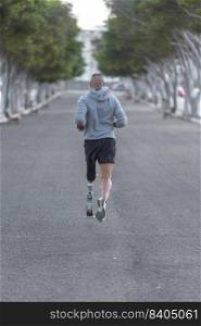 Back view of unrecognizable sportsman with prosthetic leg running along asphalt road during fitness workout in park in summer. Anonymous amputee jogging on asphalt path