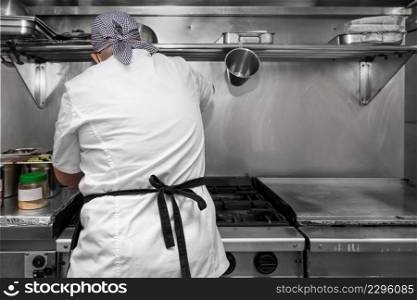 Back view of woman chef cooking food in the kitchen of a restaurant. High quality photography.. Back view of woman chef cooking food in the kitchen of a restaurant.
