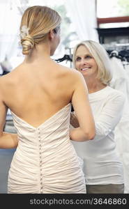 Back view of woman dressed in bridal gown with happy senior owner assisting