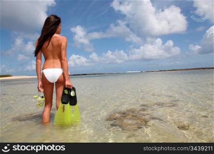 Back view of woman holding snorkeling accessories by the sea