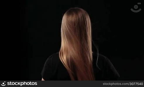 Back view of woman holding wonderful long hair and pulling her straight blond hair to show it&acute;s strength isolated on black background. Closeup rear view of blond female picking up hair in pony tail and demonstrating her strong healthy silky hair.