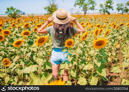 Back view of woman in a straw hat in a field of sunflowers. Summer time.. Young woman enjoying nature on the field of sunflowers.