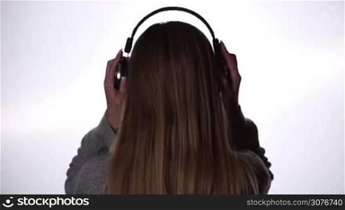 Back view of woman putting on wireless bluetooth technology headphones and listening music against white background.