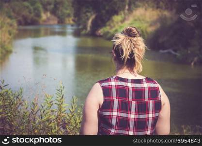Back view of woman standing and looking away at banks of the river. Relaxation and meditation concept.