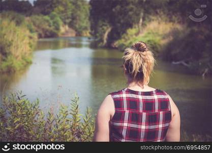 Back view of woman standing and looking away at banks of the river. Relaxation and meditation concept.