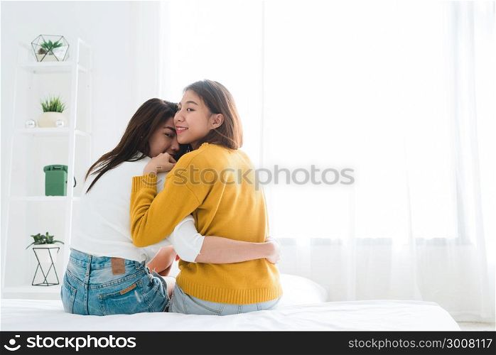 Back view of women lesbian happy couple waking up in morning, sitting on bed, stretching in cozy bedroom, looking through window. Funny women after wakeup. LGBT Lesbian couple together indoors concept