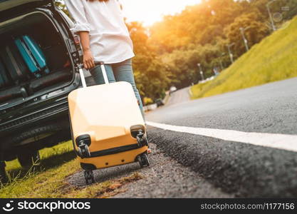 Back view of yellow suitcase dragging baggage suitcase alone road trip for loading into SUV car. People lifestyles and vacation concept. Nature and summer theme. Girl having adventure transportation