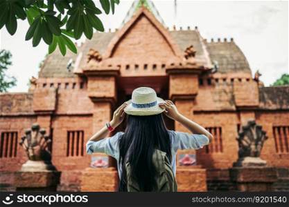 Back view of young asian backpacker woman with black long hair wearing hat standing ant looking to beautiful ancient site or Old temple during traveling on vacation