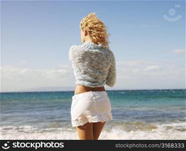 Back view of young blond woman standing at water&acute;s edge on Maui, Hawaii beach gazing at the ocean.