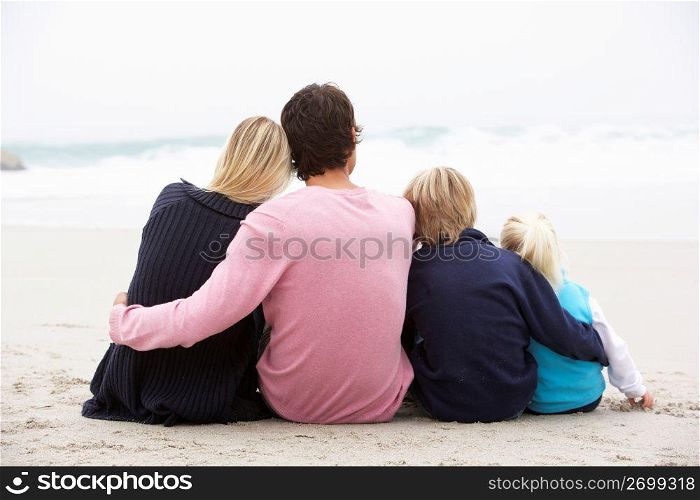 Back View Of Young Family Sitting On Winter Beach