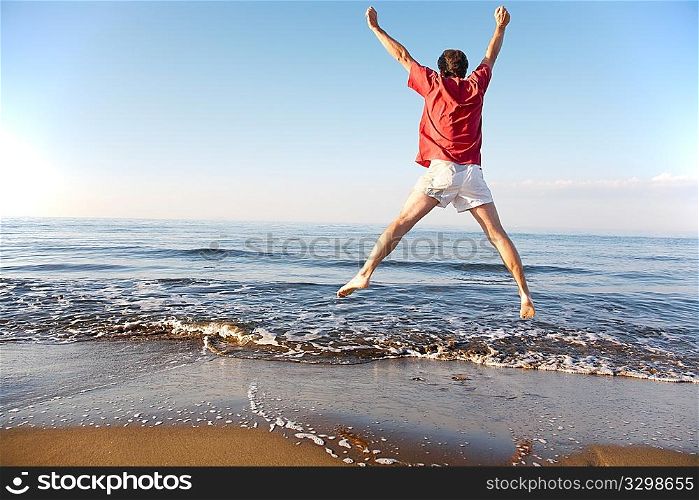 Back view of young man jumping on the beach: happiness and energy concept