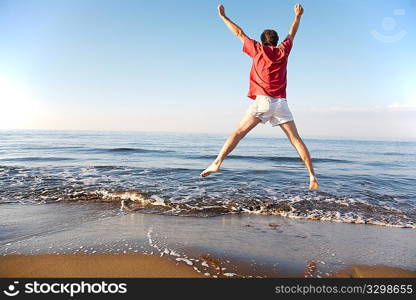 Back view of young man jumping on the beach: happiness and energy concept