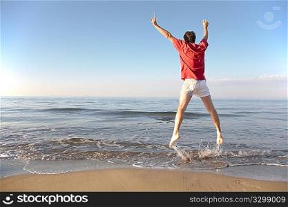 Back view of young man jumping on the beach: happiness and energy concept