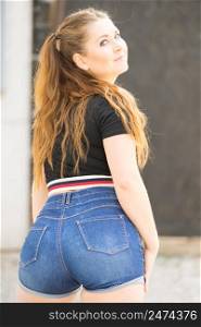 Back view of young teenage woman wearing short blue jeans denim shorts enjoying summer weather. Behind view of teenager girl