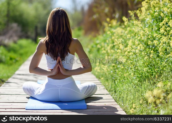 Back view of young woman doing yoga in nature. Female wearing sport clothes sitting on wooden floor.