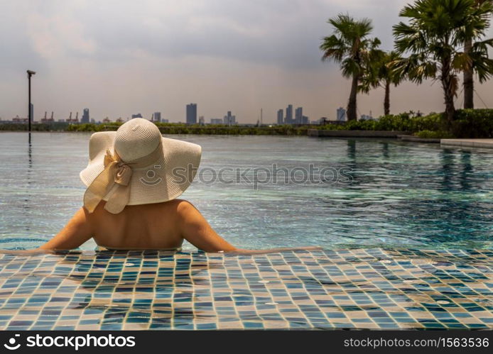 Back view of young woman in hat relaxing in swimming pool in sunny day. Summer vacation concept.