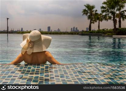Back view of young woman in hat relaxing in swimming pool in sunny day. Summer vacation concept.