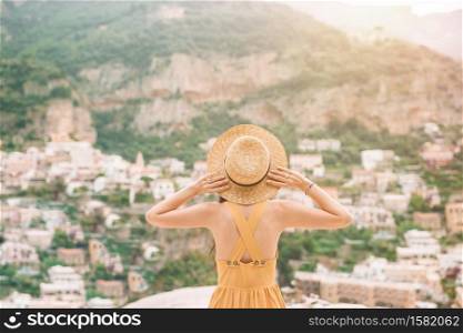 Back view of young woman in straw hat with italian village on the background, Amalfi Coast, Italy. Summer holiday in Italy. Young woman in Positano village on the background, Amalfi Coast, Italy