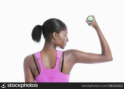Back view of young woman raising dumbbell over white background